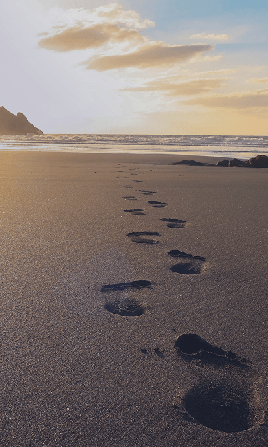 footsteps on the beach sand beneath a sunny, clear sky, representing progress and hope